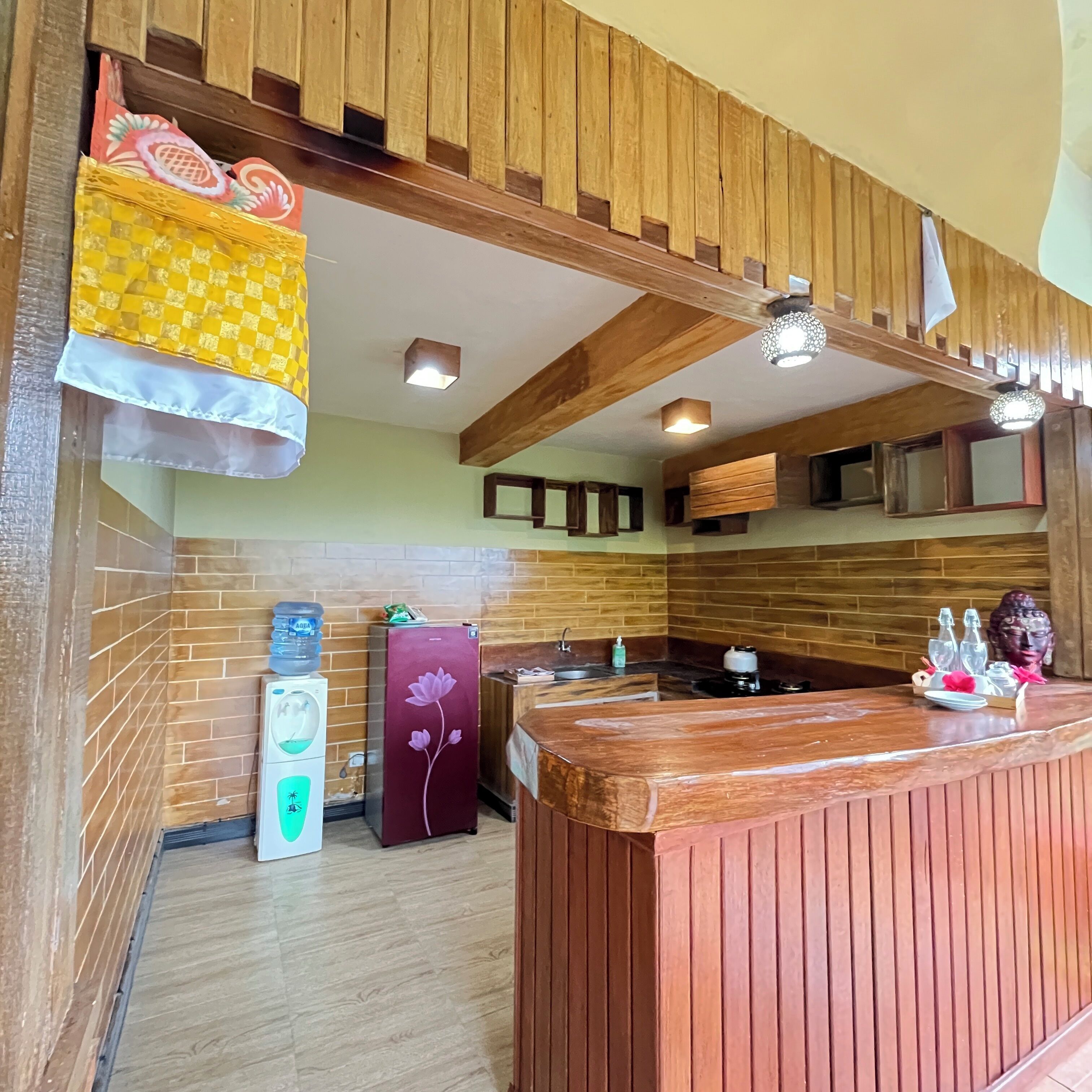 A wooden reception desk with a water dispenser, a refrigerator with a floral design, and a Buddha statue on the counter.