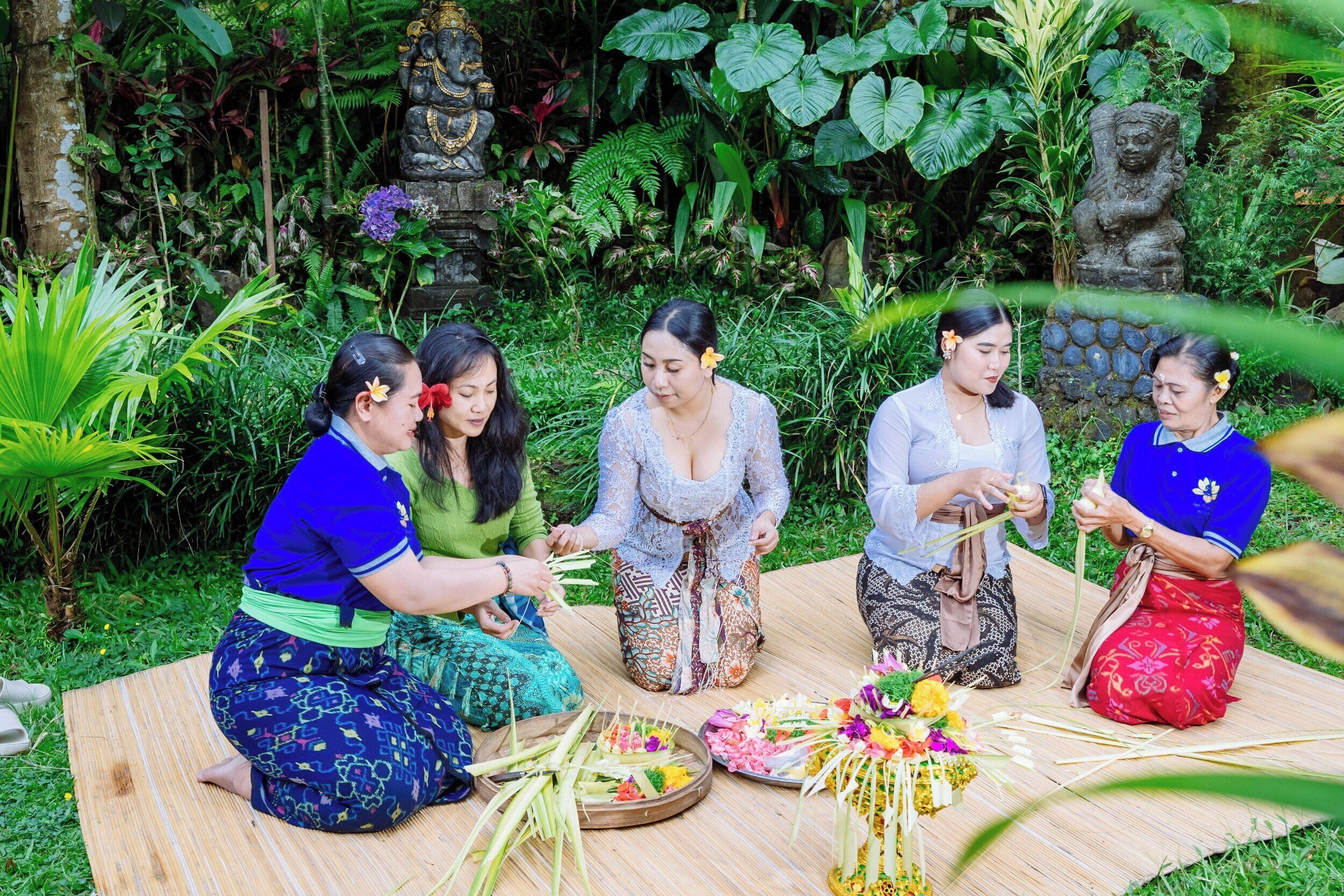 A group of people seated on a mat outdoors surrounded by greenery and stone statues.