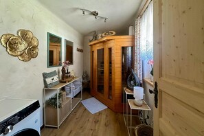 Una habitación con un armario de madera, una consola blanca con espejo y una pequeña estantería con adornos.