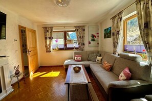 A cozy living room with a sofa, a small table, a fireplace, and a window with curtains. - Alpine Holiday Home in Lungau (Vordermuhr)