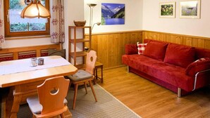 A cozy room with a wooden dining table, a red sofa, and a window with curtains. - Chalet in Königsleiten near Ski Slopes (Königsleiten)