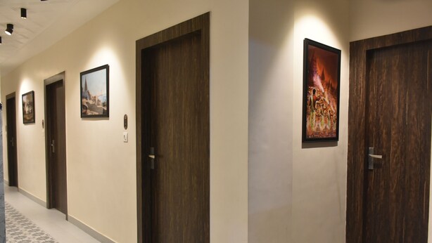 A hallway with wooden doors, framed pictures on the walls, and patterned floor tiles. - Puri Inn (Varanasi)