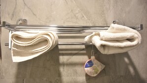 A towel rack with folded towels and a hanging bath mat in a bathroom with a marble floor. - Puri Inn (Varanasi)