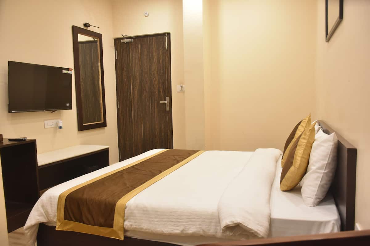 A hotel room with a bed, a bedside table, a TV mounted on the wall, and a door.
