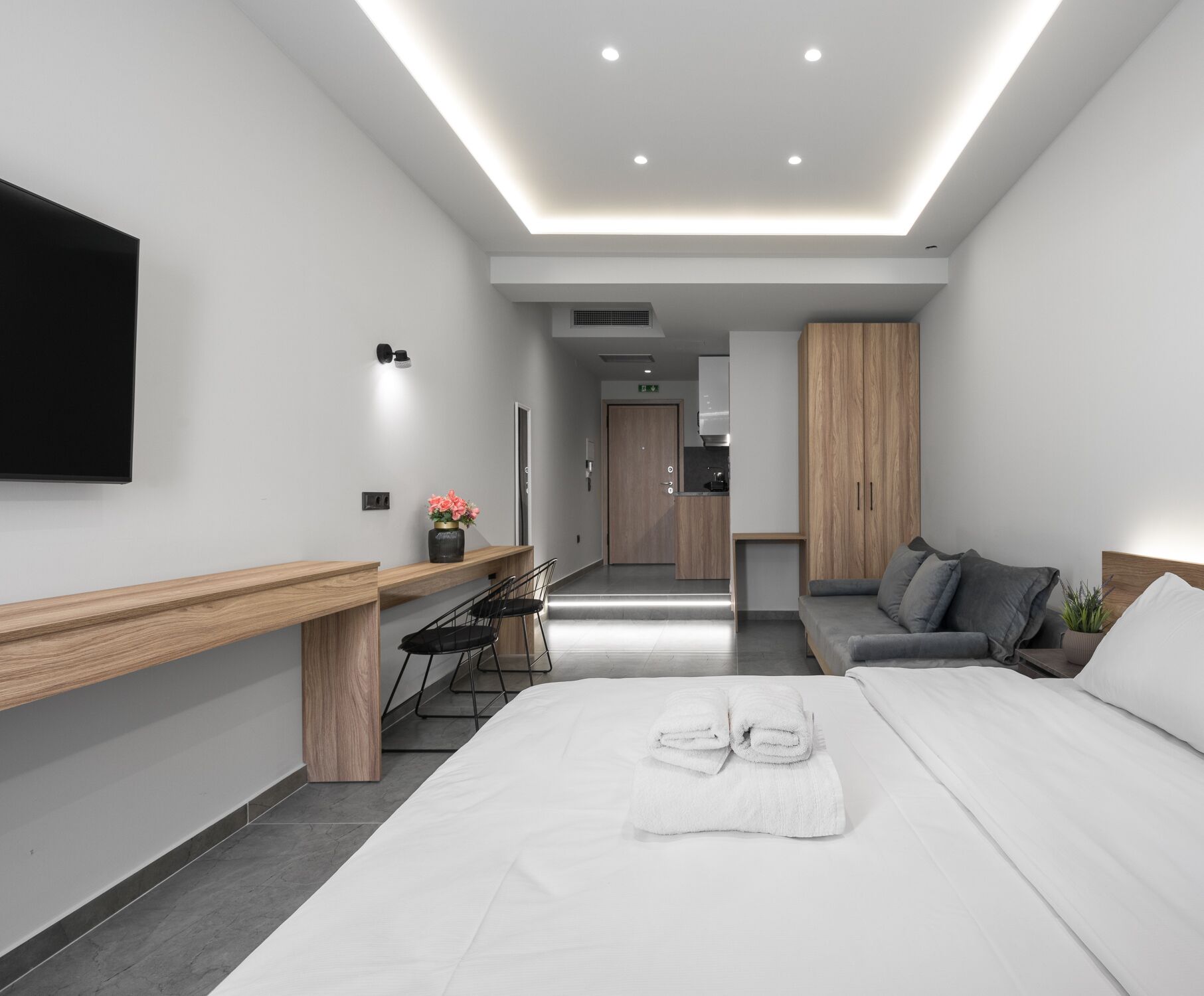 Habitación de hotel moderna con una cama, un escritorio, un sofá y una kitchenette al fondo.