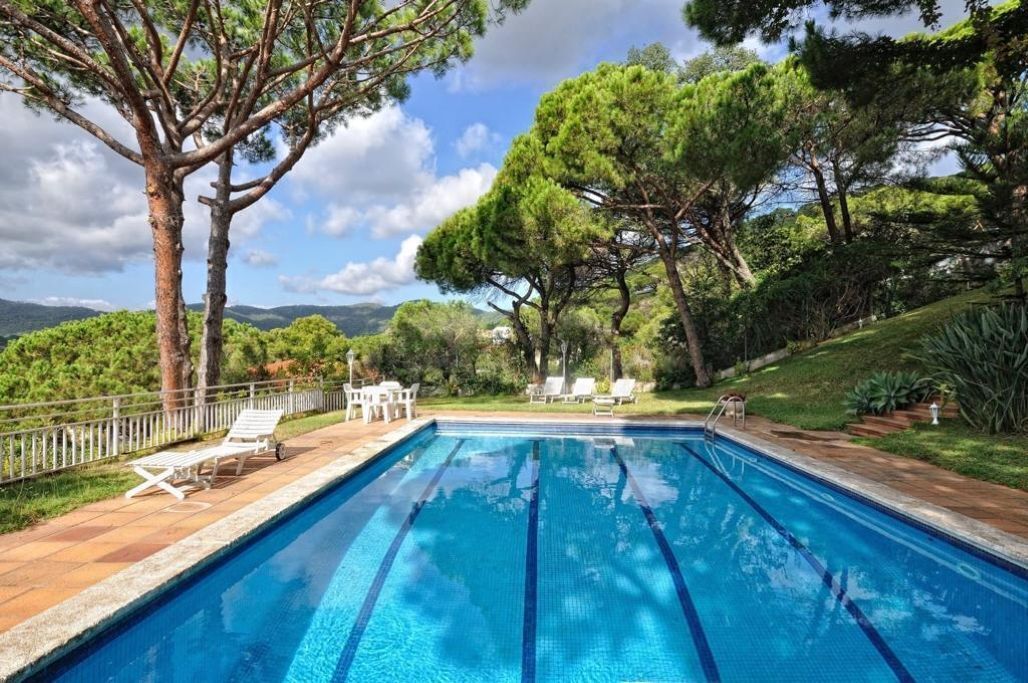 Una piscina rectangular con agua cristalina azul, rodeada por un muelle de madera y sillones blancos para tomar el sol.