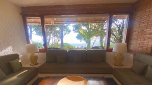 A living room with a sofa set, a wooden coffee table, and a view of trees and a body of water through large windows.