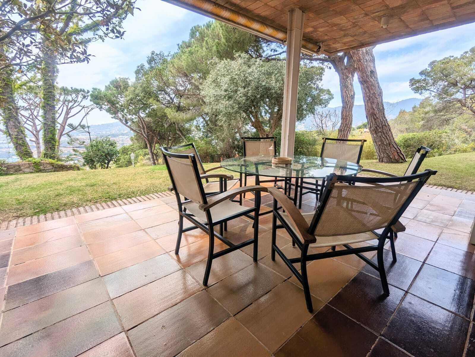 Una terrazza esterna con un tavolo e sedie in vetro, circondata da un pavimento in pietra e rigogliosa vegetazione.