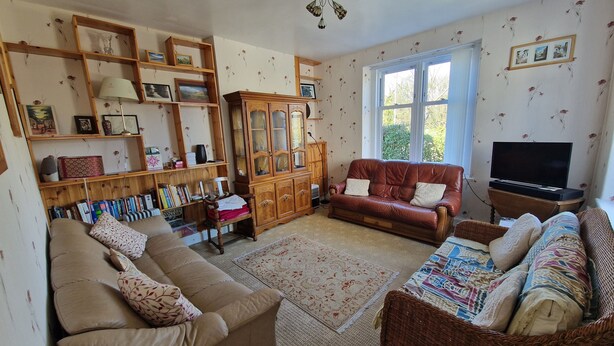 A cozy living room with a brown leather sofa, a wicker armchair, and a wooden cabinet with glass doors.