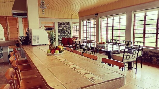 A spacious dining area with a long table and multiple chairs, large windows, and a bell hanging from the ceiling. - Villa Bonilla 12P 3C 2N (Provincia de Cartago)
