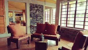 A spacious living area with a stone wall, large windows, and comfortable seating. - Villa Bonilla 12P 3C 2N (Provincia de Cartago)