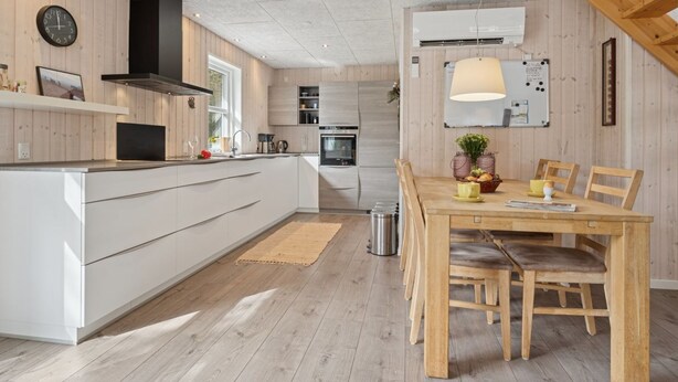 Uma cozinha moderna com ilha central, piso de madeira e área de refeições com mesa e cadeiras.
