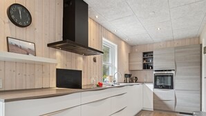 Uma cozinha moderna com armários brancos, uma coifa preta e eletrodomésticos embutidos.