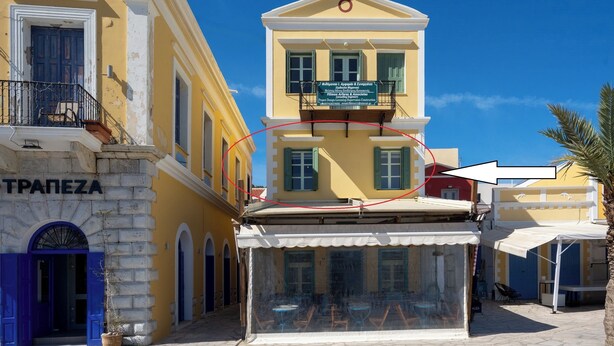 A building with a sign reading "TRAPEZA" and a balcony with a sign for "J. G. G. G. G. G. G. G. G. G. G. G. G. G. G. G. G. G. G. G. G. G. G. G. G. G. G. G. G. G. G. G. G. G. G. G. G. G. G. G. G. G. G. G. G. G. G. G. G. G. G. G. G. G. G. G. G. G. G. G. G. G. G. G. G. G. G. G. G. G. G. G. G. G. G. G. G. G. G. G. G. G. G. G. G. G. G. G. G. - Agkyra Studio in port of Symi (Simi)