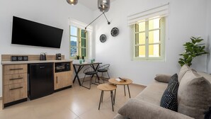A modern kitchen with a flat-screen TV, a dining area with a table and chairs, and a living room with a sofa and a plant.