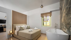 A modern bedroom with a large bed, a freestanding bathtub, and a small bedside table with a lamp. - Agkyra Studio in port of Symi (Simi)