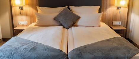 Una cama doble con cabecera de madera, dos lámparas de noche y un cojín decorativo central.