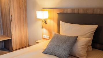 Una cama bien hecha con cabecera de madera, una lámpara de noche y una mesita de noche de madera.