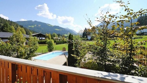 Une terrasse en bois donnant sur une piscine, avec une chaîne de montagnes en arrière-plan.