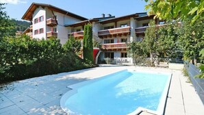 Une piscine dotée d’une terrasse en bois, entourée d’un bâtiment avec des balcons et surplombant un paysage montagneux.