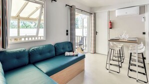 A modern room with a blue sofa, a small table with chairs, and a sliding door leading to an outdoor area. - Camping Lanterna - Eurocamp (Tar)