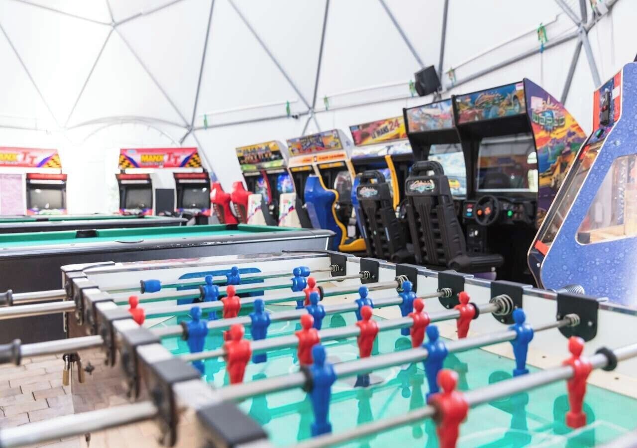 Una mesa de fútbol de mesa con jugadores rojos y azules, rodeada de máquinas de videojuegos.