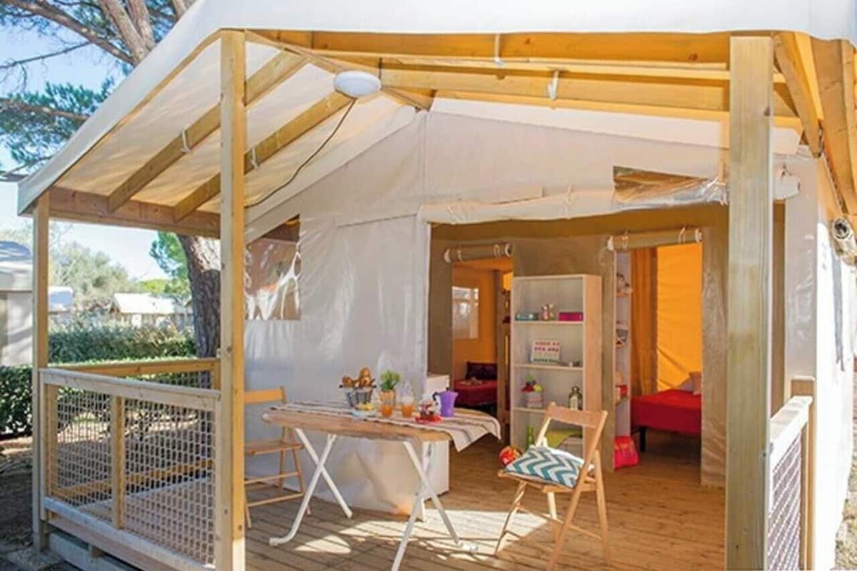 A tented outdoor area with a table, chairs, and a bookshelf.