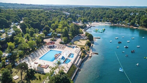 An aerial view of a resort with a large swimming pool, a marina with boats, and lush greenery surrounding the area. - Camping Lanterna - Eurocamp (Tar)