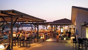 An outdoor dining area with wooden pergolas and tables, overlooking a body of water. - Camping Lanterna - Eurocamp (Tar)