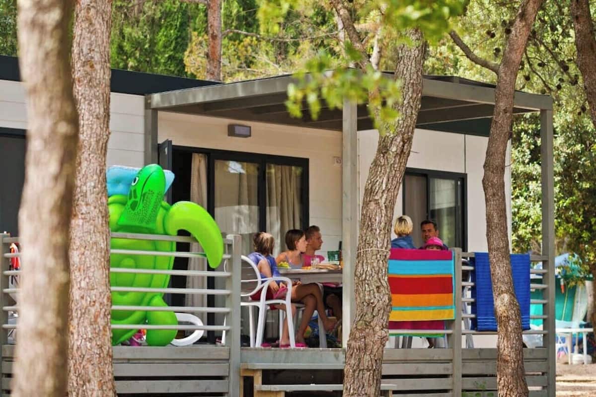 A covered outdoor seating area with tables and chairs, surrounded by trees.