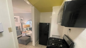 A compact kitchen with a black stove, a refrigerator, and white tiled walls. - Under the Sea (Galveston)