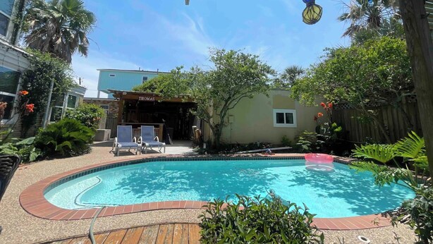 A backyard with a swimming pool, wooden deck, and outdoor seating area. - Under the Sea (Galveston)