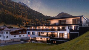 A modern multi-story hotel with a flat roof and large windows, situated in a mountainous area with a view of the Milky Way.