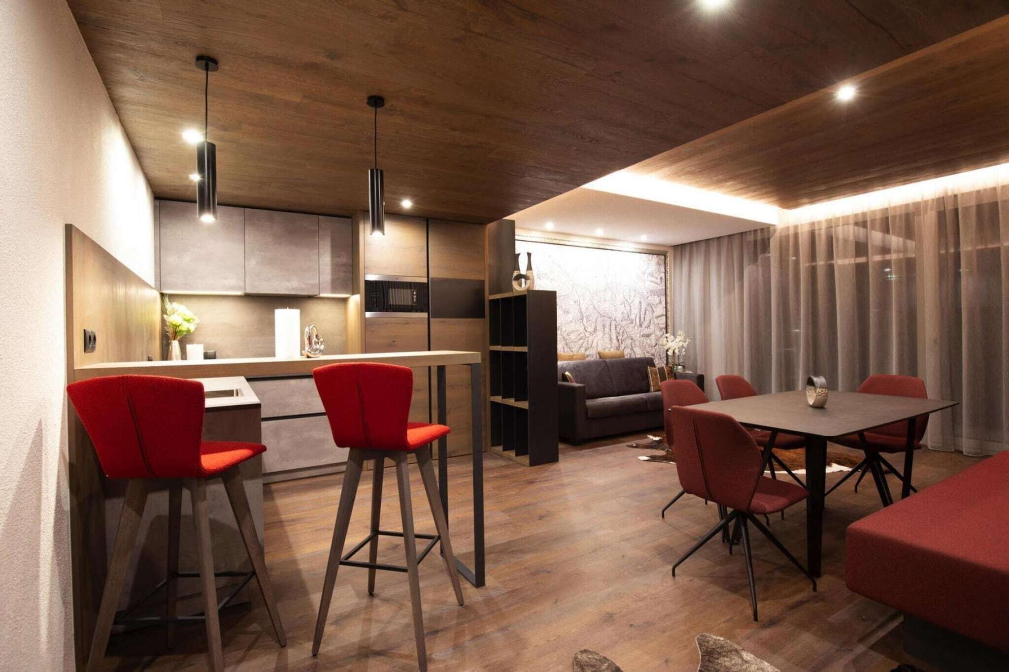 Una cocina moderna con comedor, que presenta techo de madera, sillas rojas y sofá gris.