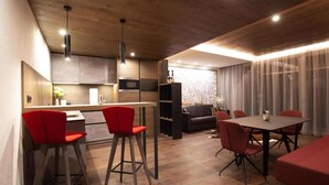 A modern kitchen with a dining area, featuring a wooden ceiling, red chairs, and a grey sofa.