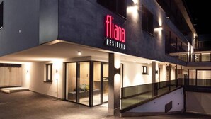 A modern building with a 'fliana residency' sign. It features a glass entrance, a staircase, and a covered outdoor area.