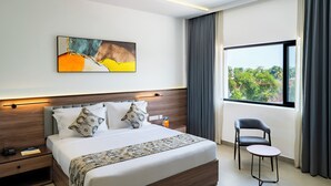 A modern hotel room with a large bed, a bedside table, a chair, and a window with a view of trees. - Hotel Hybiz by Darshan (Anchal)