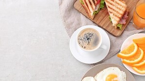 A breakfast setting with a sandwich, coffee, and eggs on a table. - Hotel Hybiz by Darshan (Anchal)