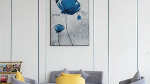 A modern living room with a grey sofa, two armchairs, a small coffee table, and a large abstract painting on the wall. - Hotel Hybiz by Darshan (Anchal)