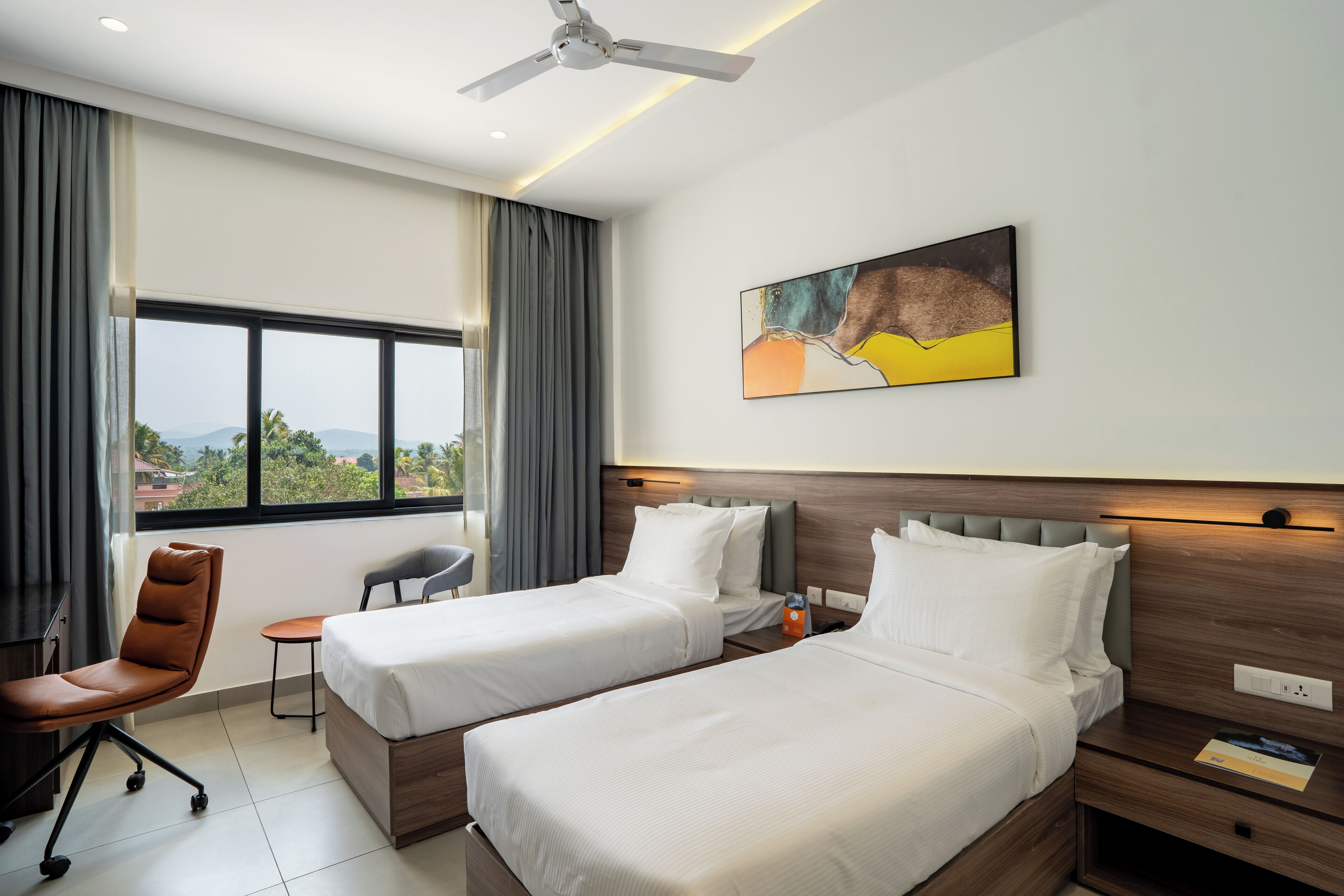 A hotel room with two beds, a desk, a chair, a small table, and a ceiling fan.