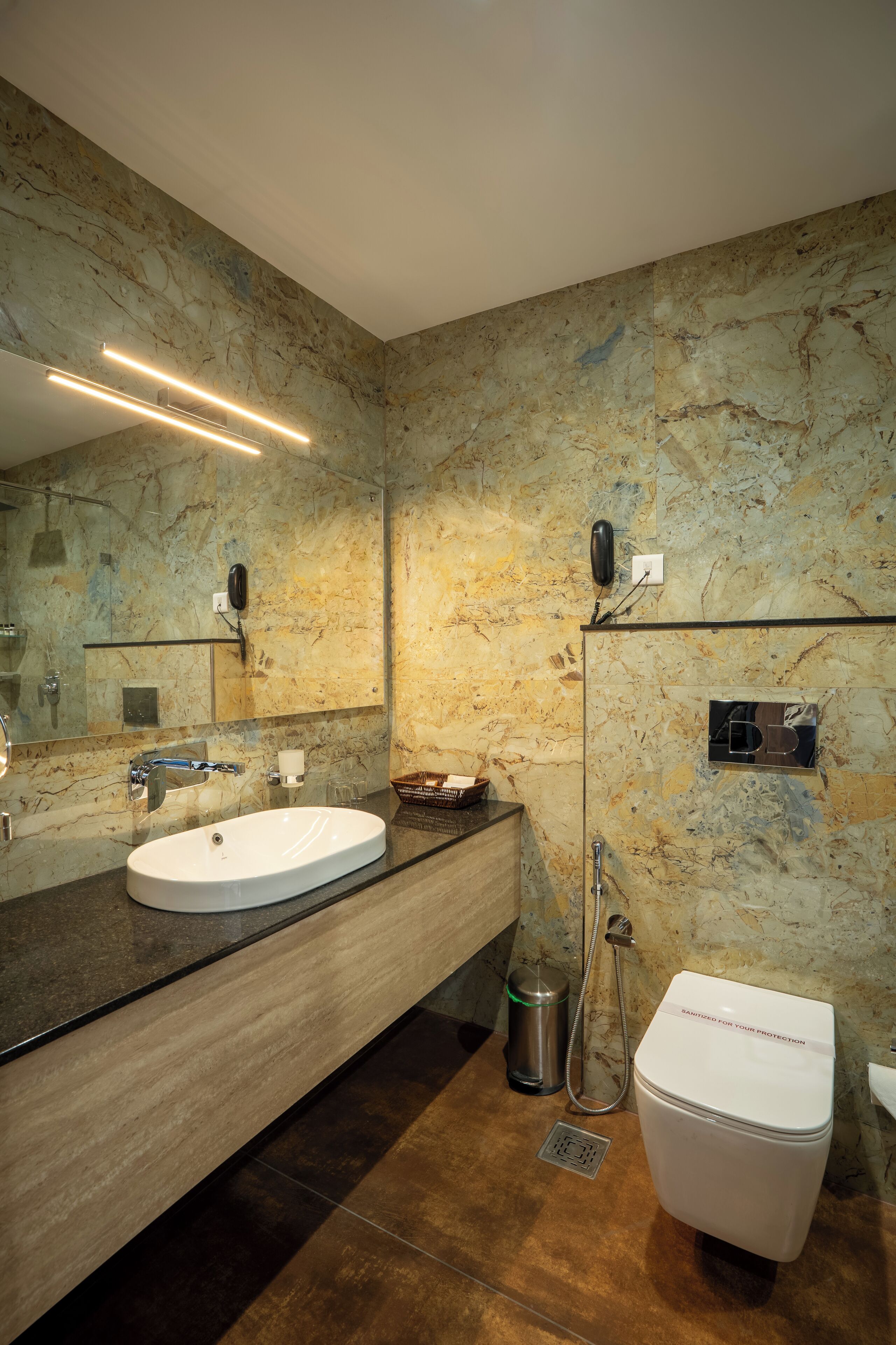 A modern bathroom with a marble wall, a sink, a mirror, a toilet, and a shower.