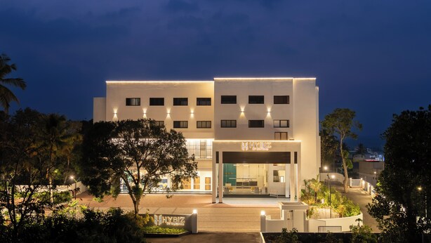 A modern hotel with a flat facade, multiple windows, and illuminated signage. - Hotel Hybiz by Darshan (Anchal)
