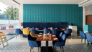 A modern restaurant with teal walls, blue and yellow chairs, and a patterned floor. - Hotel Hybiz by Darshan (Anchal)