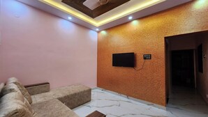 A modern living room with a sofa set, a flat-screen TV mounted on a textured wall, and a marble-patterned floor. - Relax (Bhatkal)