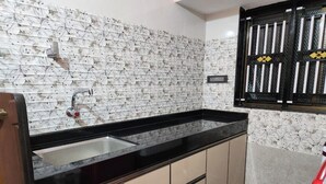 A kitchen with a black countertop, beige cabinets, and a patterned backsplash. - Relax (Bhatkal)