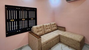 A beige sectional sofa against a pink wall with a window featuring vertical bars and a decorative design. - Relax (Bhatkal)