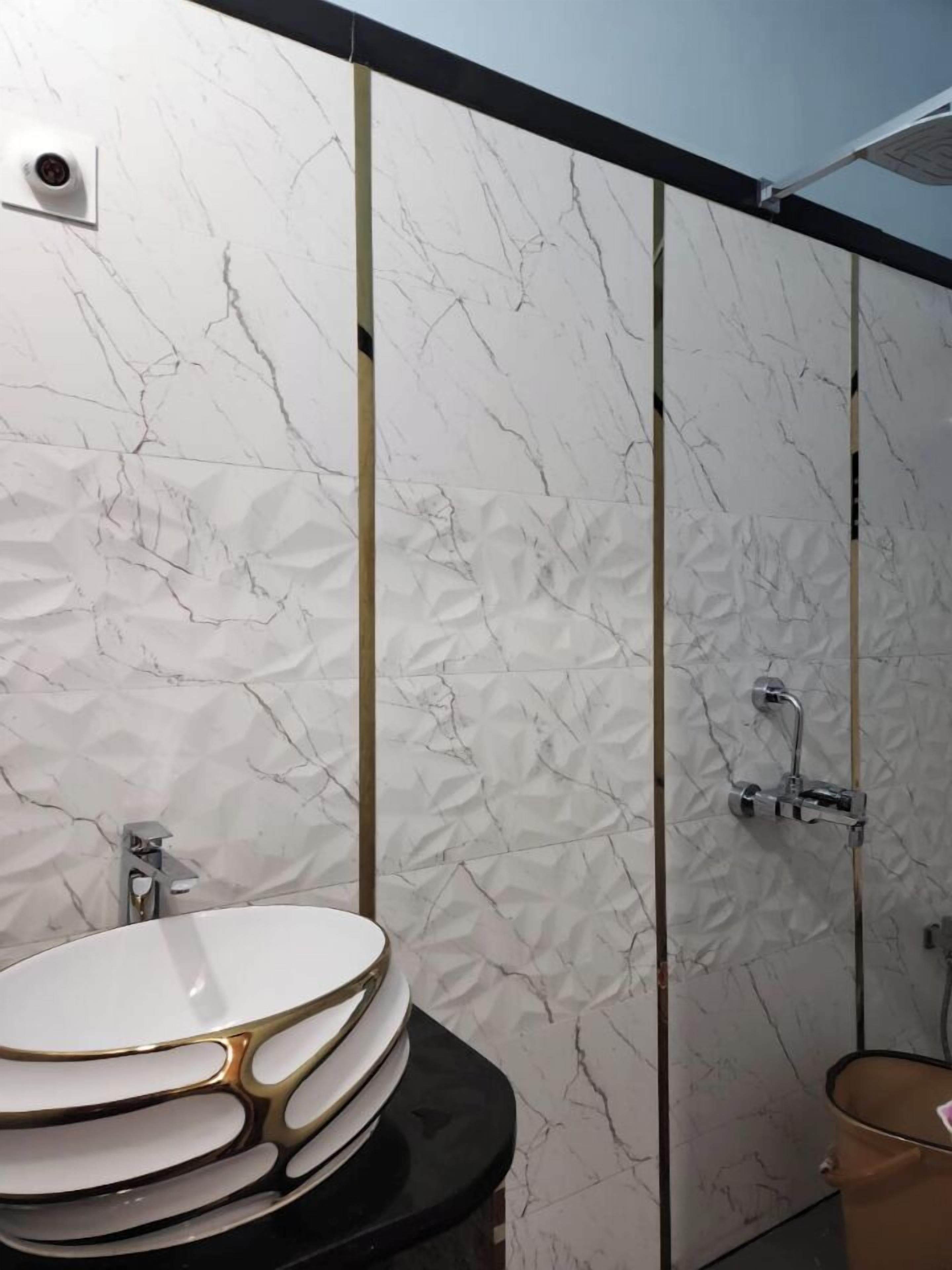 Ein Badezimmer mit einer weißen Marmorwand, einer schwarzen Ablage und einem goldfarbenen Waschtisch.
