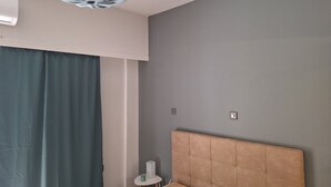 Un dormitorio con una cama, una pared gris, una lámpara en el techo y una mesita con una vela.