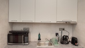 Una cocina compacta con microondas, cafetera y un lavamanos pequeño.