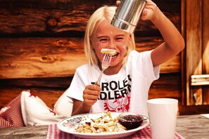 Une personne est assise à une table en bois, devant une assiette de nourriture, une tasse blanche et une serviette à carreaux.